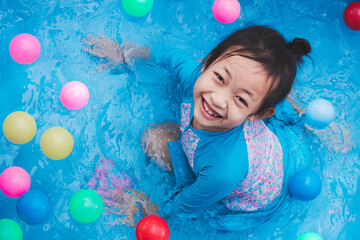 Fototapeta na wymiar A brightly smiling little girl in a swimming suit splashes in the rubber pool with joy and happiness in summertime at home