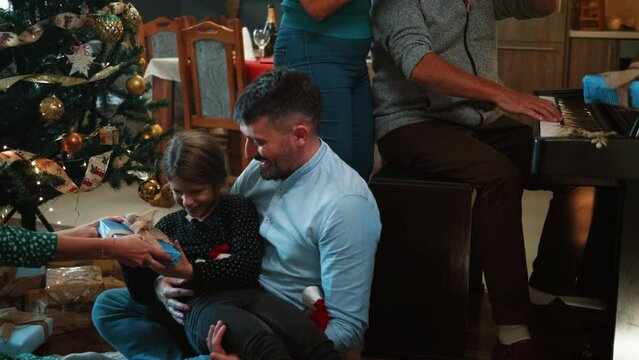 Adult parents play with a child while grandparents toast with champagne at a joint Christmas celebration