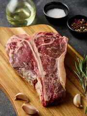 Raw fresh beef T-bone steak with rosemary, salt and pepper.