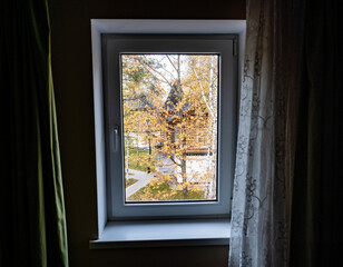 autumn landscape with yellow trees against the background of wooden houses in the window frame from the room