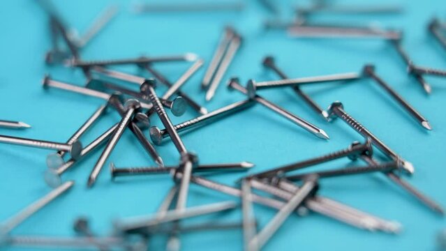Industrial steel nails falling on a creative colored blue background. Carpentry tool close-up. Slow motion. Rotation