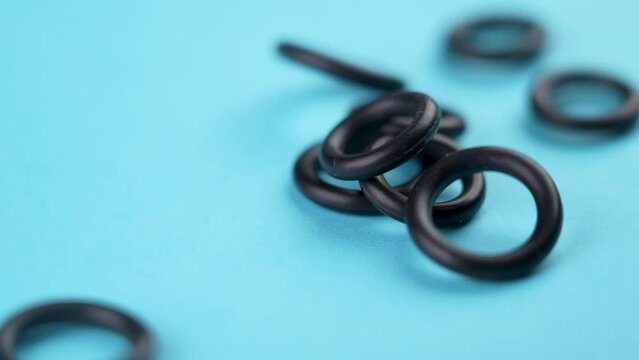 Black elastic rubber o-rings with a round geometric shape falling on a colored blue background in slow motion. Rotation