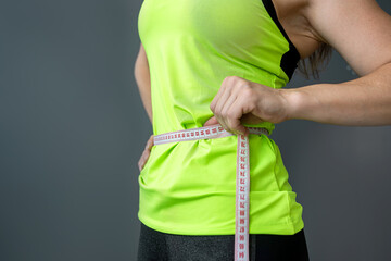 slim woman measuring her waist with a tape measure after dieting isolated on gray background.