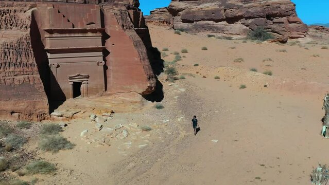 Aerial view of a man walking in front of Nabataean city tombs of Hegra in Saudi Arabia - circling, drone shot