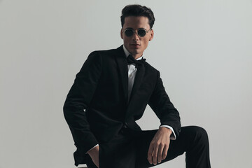 sexy young groom in black tuxedo wearing sunglasses and holding hand in pocket
