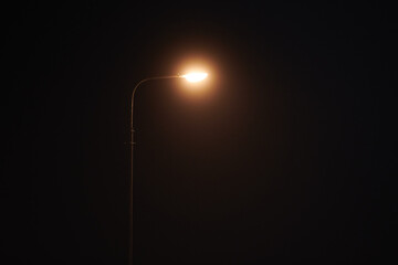 One night lamppost shines with faint mysterious yellow light through evening fog. Streetlight shine...