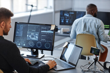 Portrait of male programmer or data specialist using computer in office with charts on screen, copy...