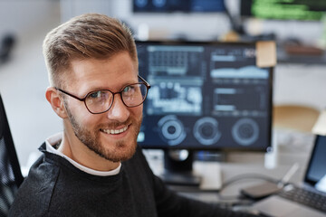 Close up portrait of young software developer smiling at camera and wearing glasses in office, copy...