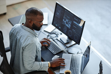 Minimal high angle view at African American software developer working with computers and data systems in office - Powered by Adobe