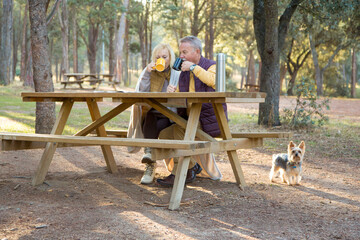Mature couple with a dog drinking coffee in a picnic area in the forest