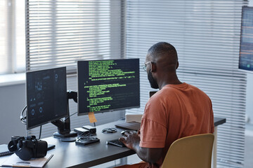 Minimal back view of African American man writing code in green lines and using computers in...