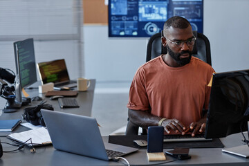 Portrait of young black man using computer in high technology office, data systems and programming...