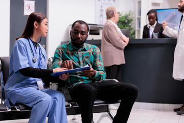 Medical trainee taking personal data from african american patient before admitting him to medical consultation at hospital. Receptionist attending elderly woman, general practitioner at clinic