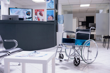 Orthopaedic wheelchair in front of waiting chairs at medical clinic reception desk. Chair for people without mobility with no one occupying it in empty waiting room of hospital with no patients.