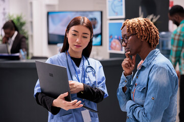 Asian general practitioner using computer to give care instructions to young african american woman...