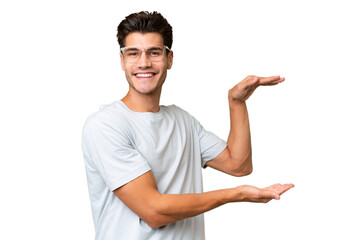 Young caucasian handsome man over isolated background holding copyspace to insert an ad