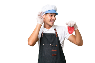 Butcher caucasian man wearing an apron and serving fresh cut meat over isolated background listening to something by putting hand on the ear