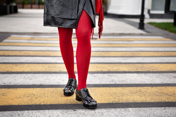 Woman legs in red color tights, black leather shoes with rivets and skirt stand on crosswalk....