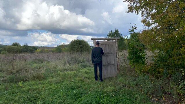 Person exits via the door that leads to nowhere and disappears. Man going through old mystery portal in the open field. Concept of finding a way out, existence of the supernatural or another world