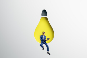 Abstract image of attractive young european businessman sitting on abstract hanging light bulb chair and using laptop on white background. Idea, innovation, work culture and inspiration concept.