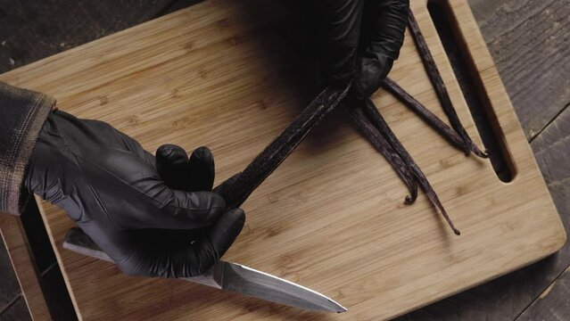 Top view of a male wearing nitrile gloves showing inside of vanilla pod seeds on a cutting board
