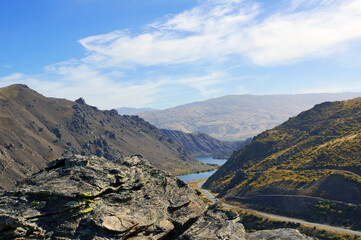 Fototapeta premium View of the Cromwell Gorge and Lake Dunstan from high up on the cycling track on a blue sky Autumn day. Shist rocks in foreground.