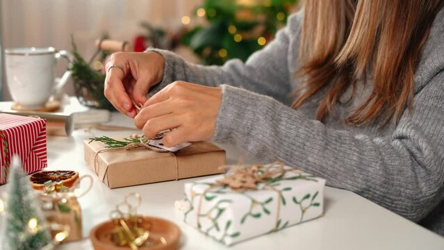 Woman s hands wrapping Christmas gift boxes, close up. Unprepared presents on white table with decor elements and items Christmas or New year DIY packing Concept.