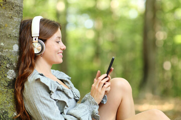 Happy woman listening to music relaxing in a forest