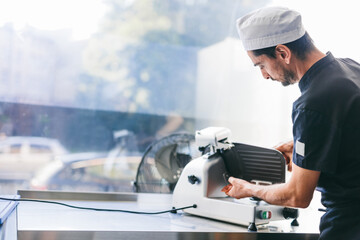 Italian chef slicing ham for pizza in restaurant kitchen