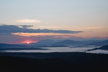 The beginning of a new day dawn in the mountains the sun rises on the horizon, the morning fog, smoke filled the river valley.