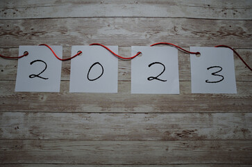 New year 2023 design on wooden background with written papers and red ribbon.