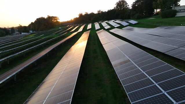 Sunlight reflects on glossy solar panels during golden hour sunset. Aerial view. Green renewable energy, global warming theme.