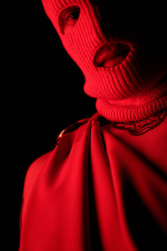 Close-up of young gangster in balaclava standing in dark against black background