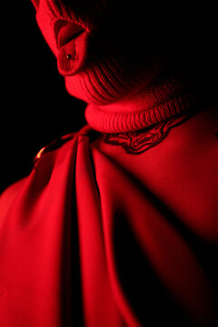 Close-up of man in balaclava with showing piercing in his tongue posing in dark studio