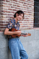Young Asian man smiling and playing acoustic Ukulele guitar at street.