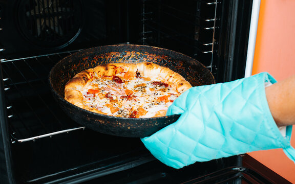 Close-up Of Hand Taking Out Of Oven Pizza With Mozzarella Cheese And Basil In Frying Pan, Hot Traditional Food Of Italian Home Cooking