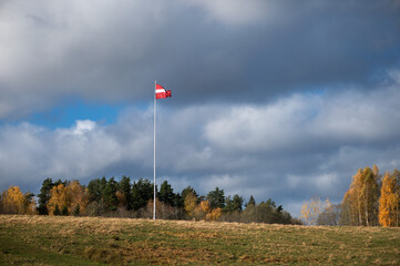Latvian national flag flutters raised on a tall mast against the background of autumn nature and...