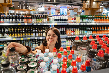 Positive glad beautiful female in the shop want to buying bottle with water