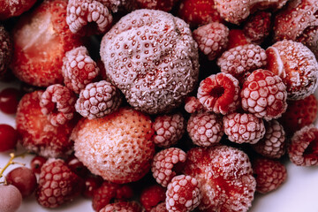 Red frozen berries covered with frost on white plate. Raspberries, strawberries, red currants. Preservation of summer vitamins for winter, conservation and storage of crops