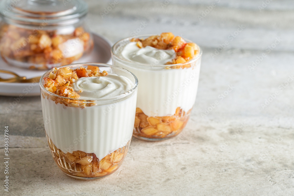 Sticker Greek yogurt with caramelized cinnamon apple and walnuts, dessert on light stone table.