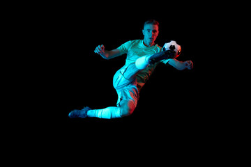 Dynamic shot of young active football player in action isolated on dark background in neon light....