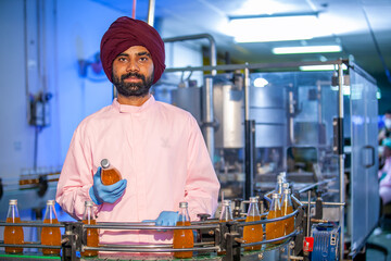 Asian man worker with clipboard is checking product bottles of fruit juice on the production line in the beverage factory. Manufacturer checks quality of food industry.