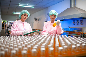 Asian woman worker with clipboard is checking product bottles of fruit juice on the production line in the beverage factory. Manufacturer checks quality of food industry. - 540638110