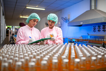Asian woman worker with clipboard is checking product bottles of fruit juice on the production line in the beverage factory. Manufacturer checks quality of food industry. - 540638117