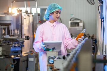 Asian woman worker with clipboard is checking product bottles of fruit juice on the production line in the beverage factory. Manufacturer checks quality of food industry. - 540638130