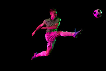 Young professional male football soccer player in motion isolated on dark background in neon light. Concept of sport, goals, competition, league, ad.