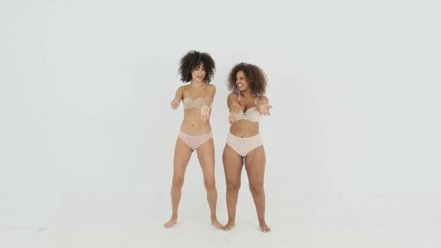 Delighted black young ladies in lingerie dancing in light studio
