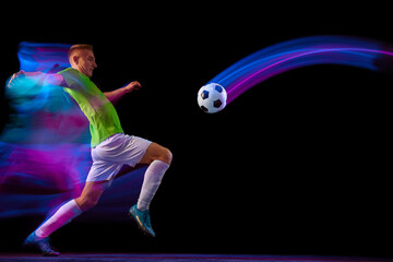 Fototapeta na wymiar Sport in action. One man professional soccer player training with football ball isolated on dark background in neon light filter. Sport, speed, power and energy