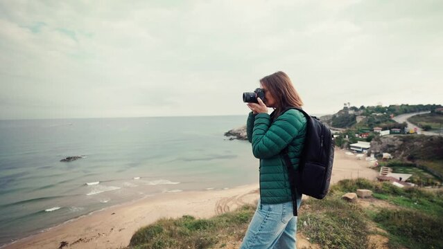 Slow-motion footage of a woman photographer taking pictures of the seascape with a camera while traveling.