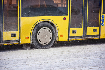 Bus riding on snow covered road, snowfall on city road. Public yellow bus wheel in the city on...